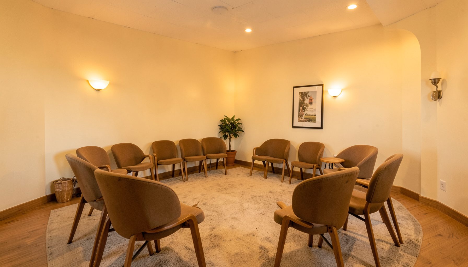 Warmly lit community meeting space with chairs arranged in a circle, cream walls and soft amber lighting, welcoming and inclusive atmosphere