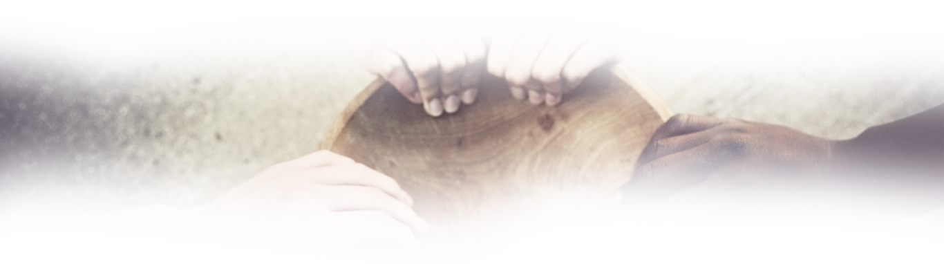Three hands of different skin tones resting together on a round wooden drum surface, warm muted tones, unity and togetherness